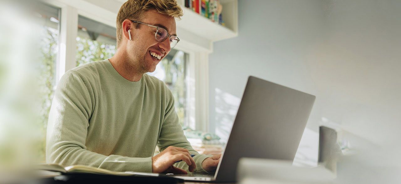 ein lächelnder Mann sitzt an einem Tisch mit einem Laptop